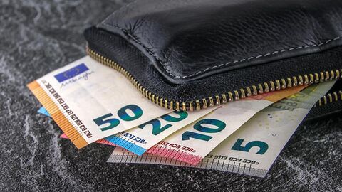 Vier verschiedene Geldscheine ragen fächerförmig aus einer schwarzen Geldbörse heraus.