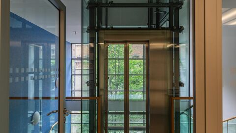 Durch eine geöffnete Glastür ist ein menschenleerer Flur zu sehen.