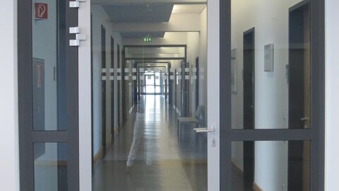 Durch eine gläserne Tpr kann man einen langen Flur mit zahlreichen abgehenden Türen sehen.
