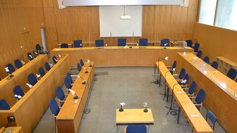 Sitzngssaal 165 C Gezeigt wird ein leerer Sitzungssaal mit Blick auf die Richterbank, dahinter eine Leinwand.