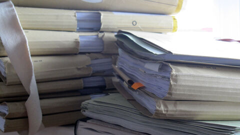 Zwei unterschiedlich hohe Aktenstapel liegen auf einem Tisch.