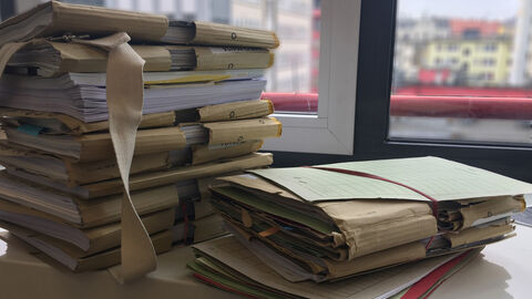 Zwei unterschiedlich hohe Aktenstapel liegen auf einem Tisch vor einem Fenster.