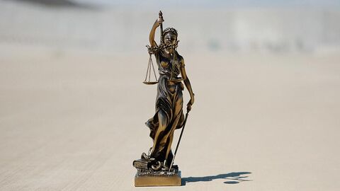 Justitiastatue steht auf einem sandigen Boden und wirft Schatten.