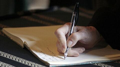 Hand hält einen Kugelschreiber und schreibt in ein Heft.