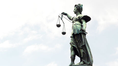 Justitia Statue vor einem hellen Himmel.