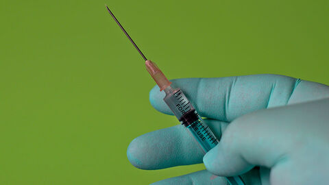 Eine Hand in Latexhandschuhen hält eine Spritze mit einer Flüssigkeit.