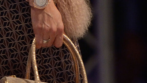 Person hält mit einer Hand die goldfarbenen Träger einer Handtasche.