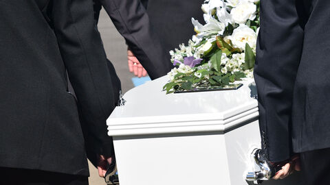 Sargträger tragen einen weißen, mit Blumen geschmückten Sarg.