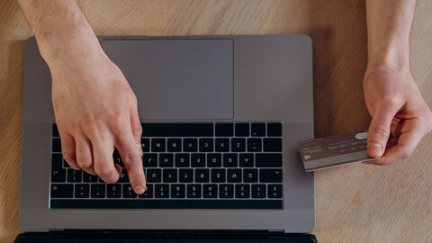 Mann tippt mit einer Hand auf einer Notebook-Tastatur und hält eine Bank- oder Kreditkarte in der anderen.
