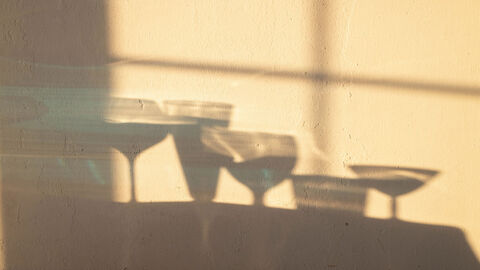 Schatten mehrerer Stielgläser an einer Wand.