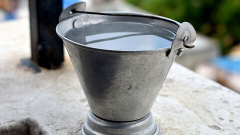 Ein Eimer gefüllt mit Wasser steht auf einer Balkonbrüstung.