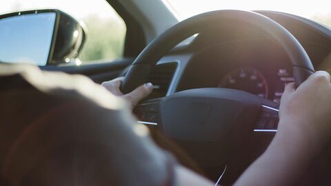 Blick über die Schulter einer in einem Auto sitzenden Person auf ein Lenkrad