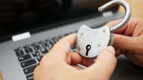 Zwei Hände halten ein offenes Vorhängeschloss vor einer Laptop-Tastatur.
