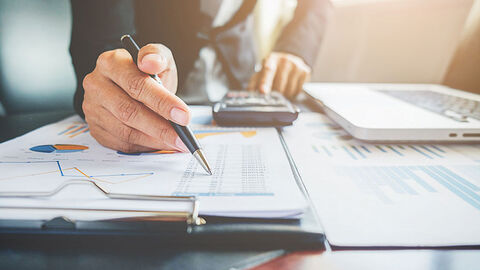 Jemand sitzt an einem Schreibtisch und rechnet.